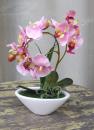 Künstliche Orchidee mit rosa Blüten im ovalen Gefäß